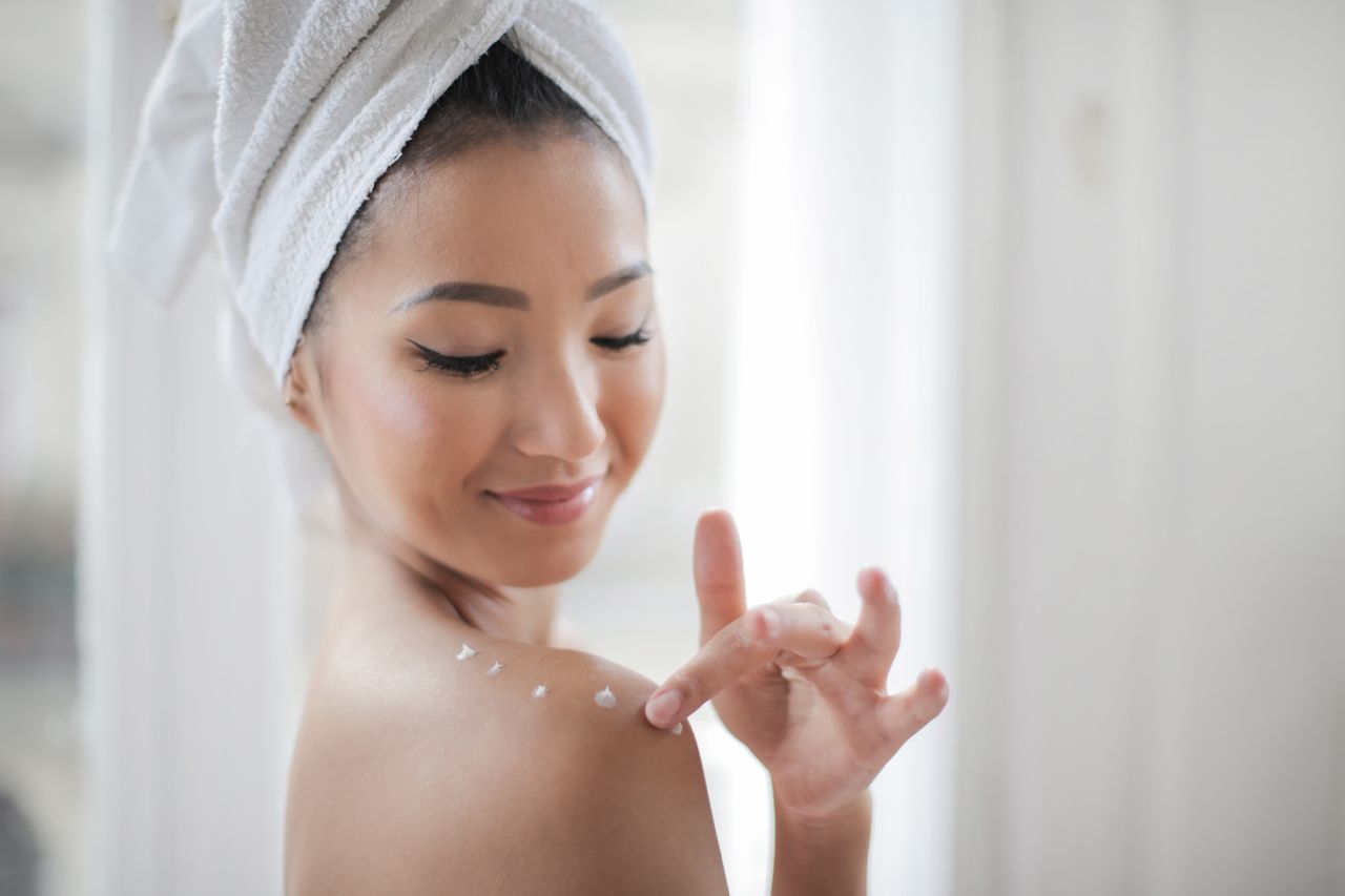 our-services-02 A young woman applying moisturizer indoors, enhancing skin care routine.